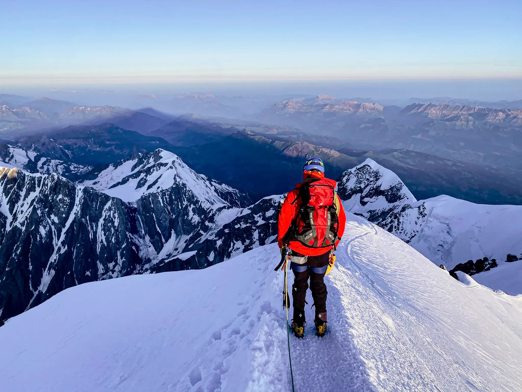 Alpiniste au sommet du Mont Blanc, face à un panorama majestueux de montagnes enneigées.