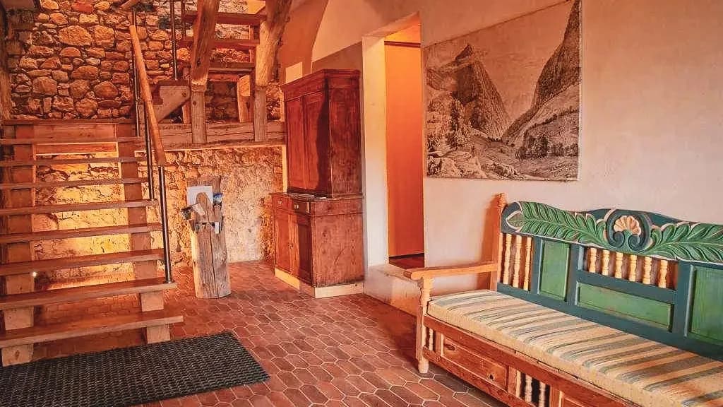 Un hall accueillant avec un escalier en bois, des murs en pierre et un canapé coloré, parfait pour se détendre après le trail.