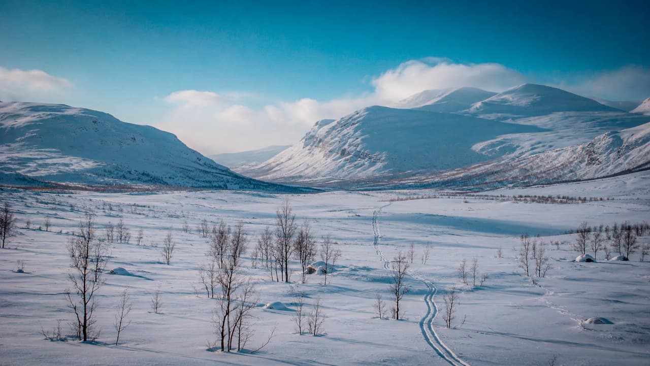 Panoramisch uitzicht op de Kungsleden: besneeuwde landschappen en majestueuze bergen schitteren onder de blauwe hemel.