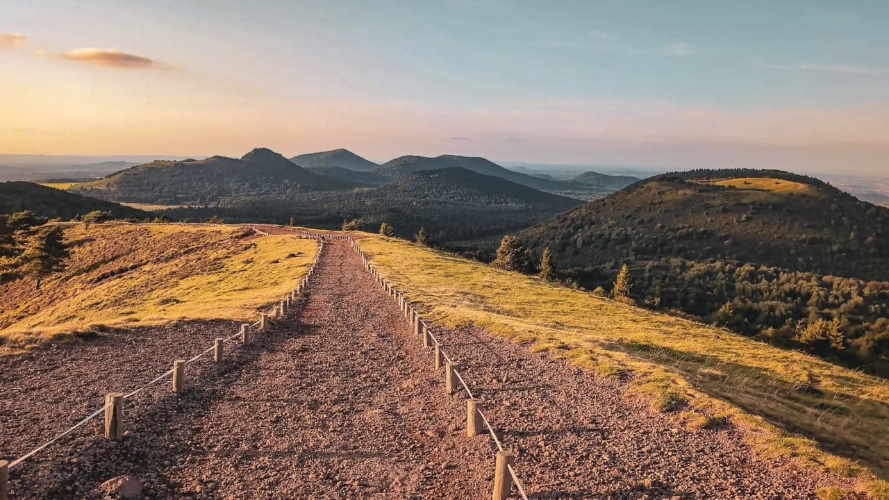 A picturesque path winds through the volcanic hills of the Auvergne, under a golden sky.