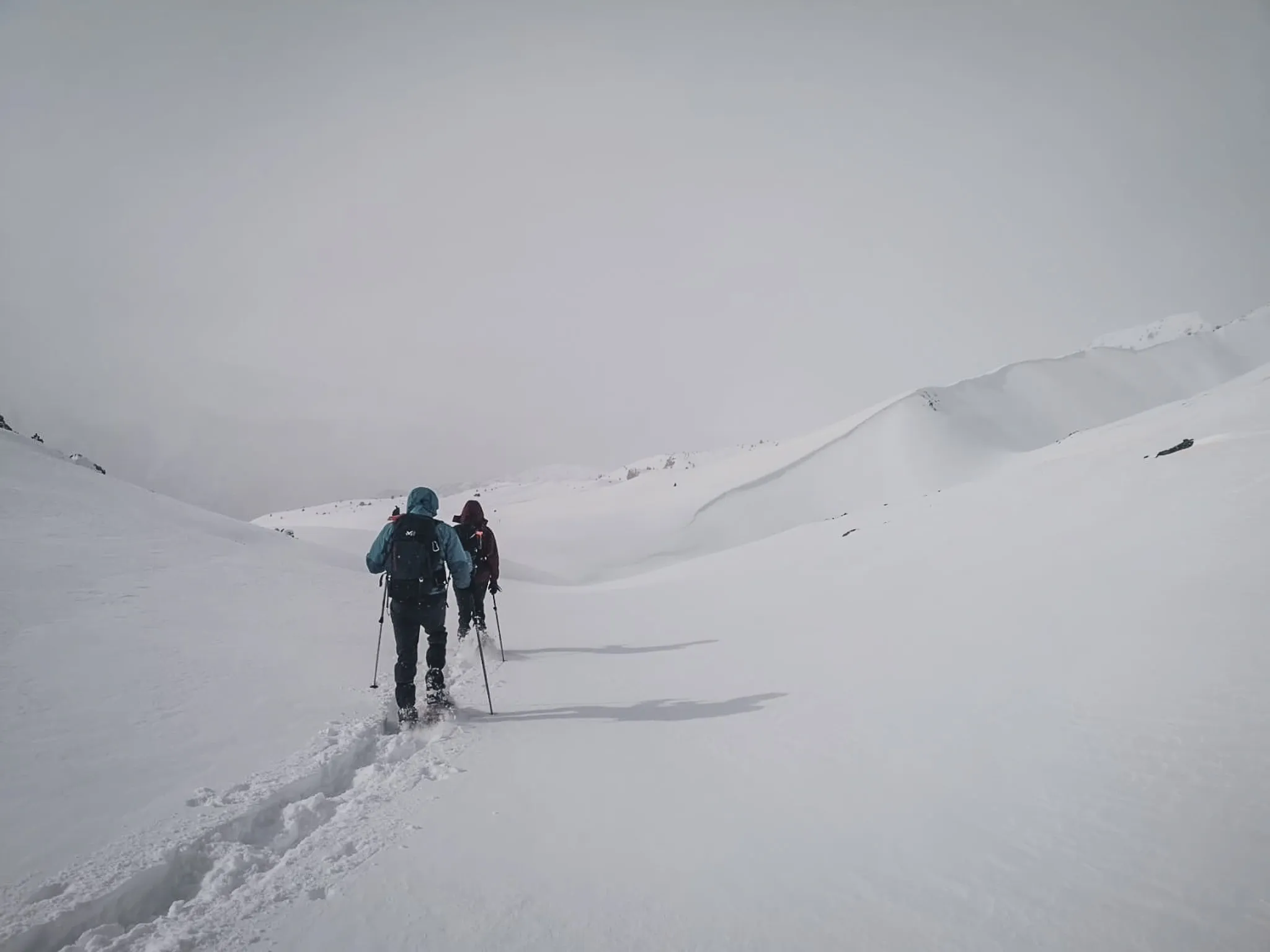 Two walkers on snowshoes make their way through a snow-covered landscape, between ridges and tranquillity.