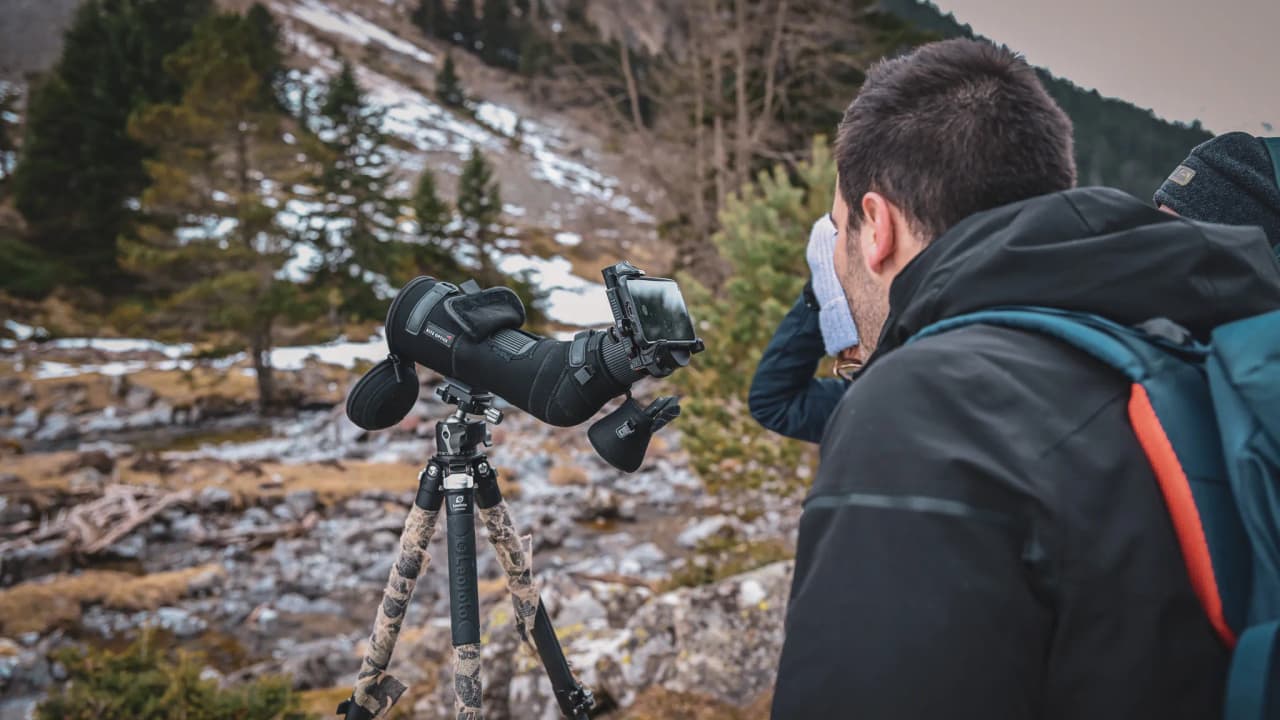 A participant observes wildlife using professional equipment, surrounded by snow-covered landscapes in the Pyrenees.