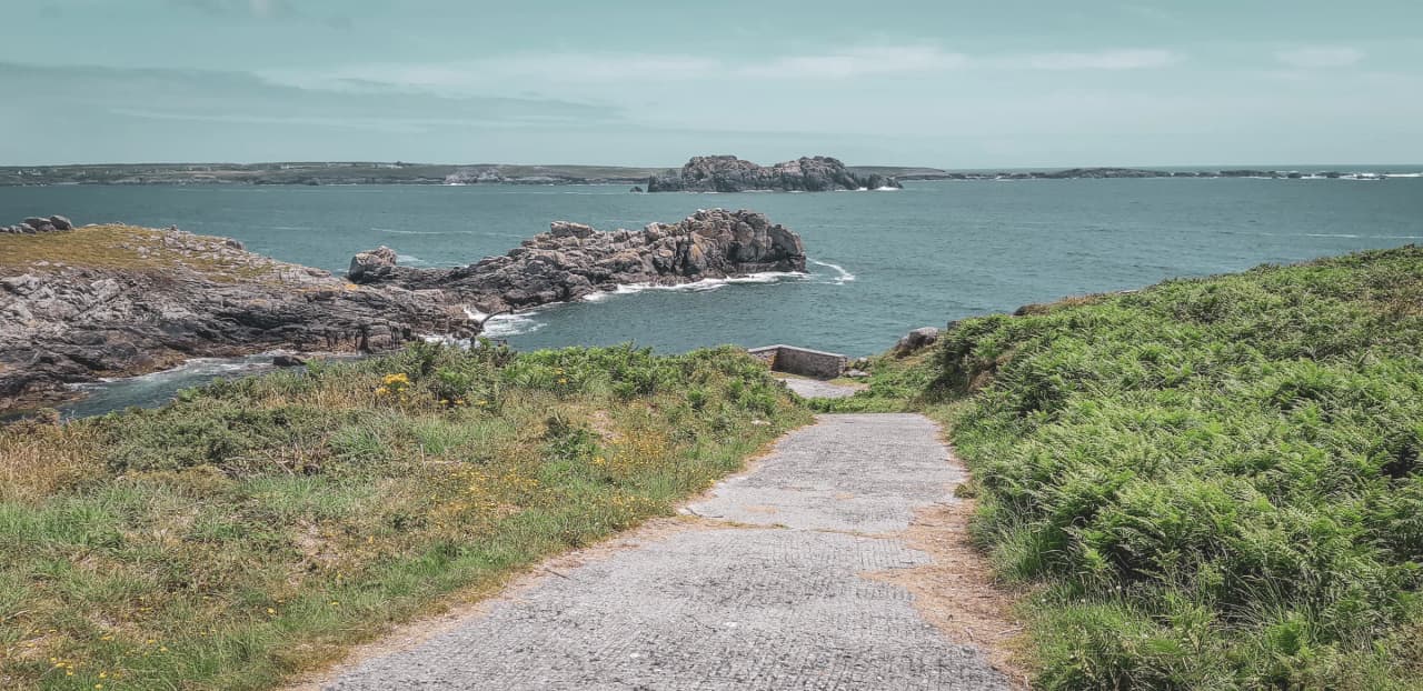 A winding path leading down to the sea, surrounded by greenery and rocky outcrops, an invitation to adventure.