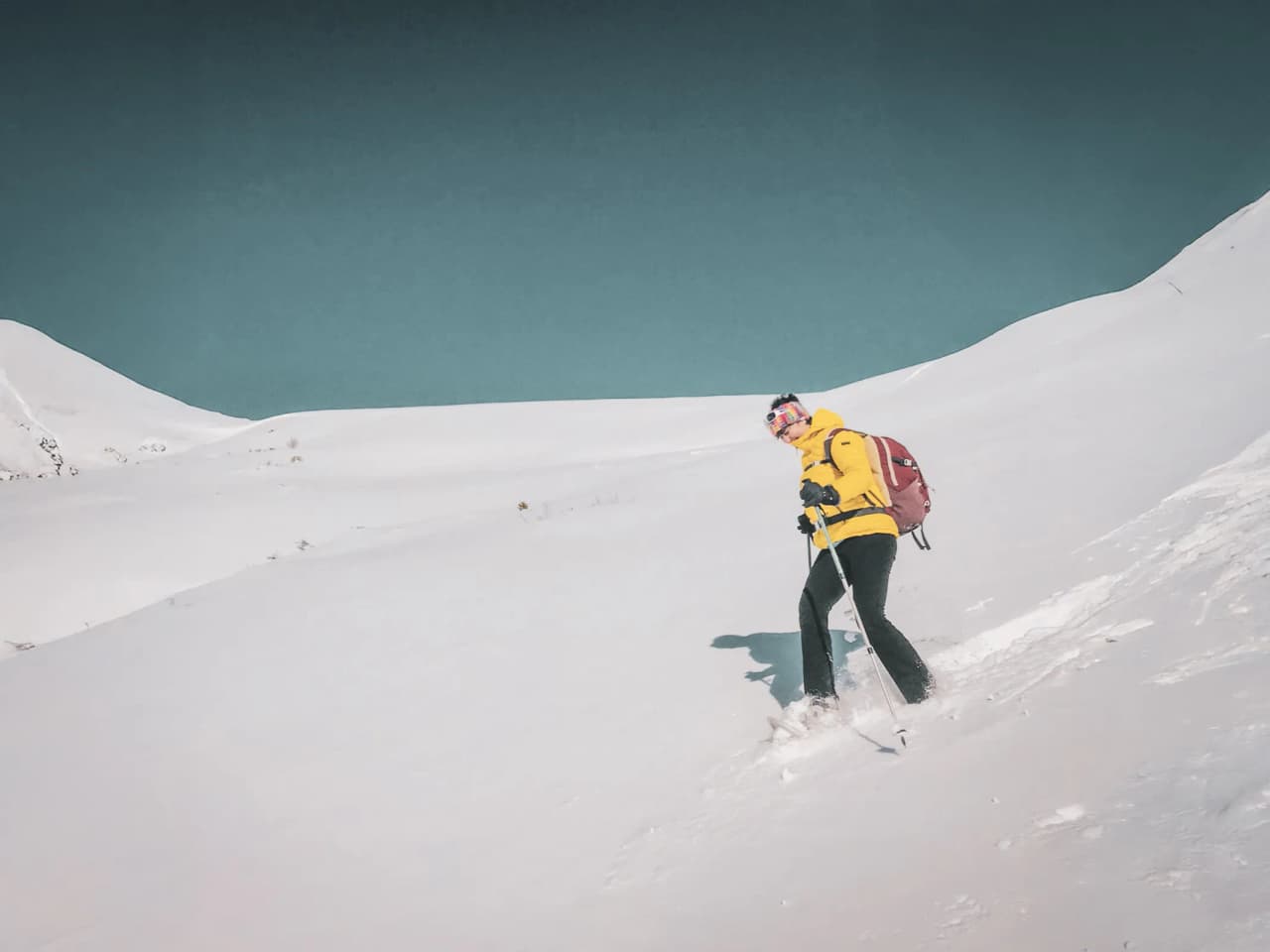 Randonneur en raquettes, vêtue de jaune, explore un paysage enneigé face aux glaciers majestueux.