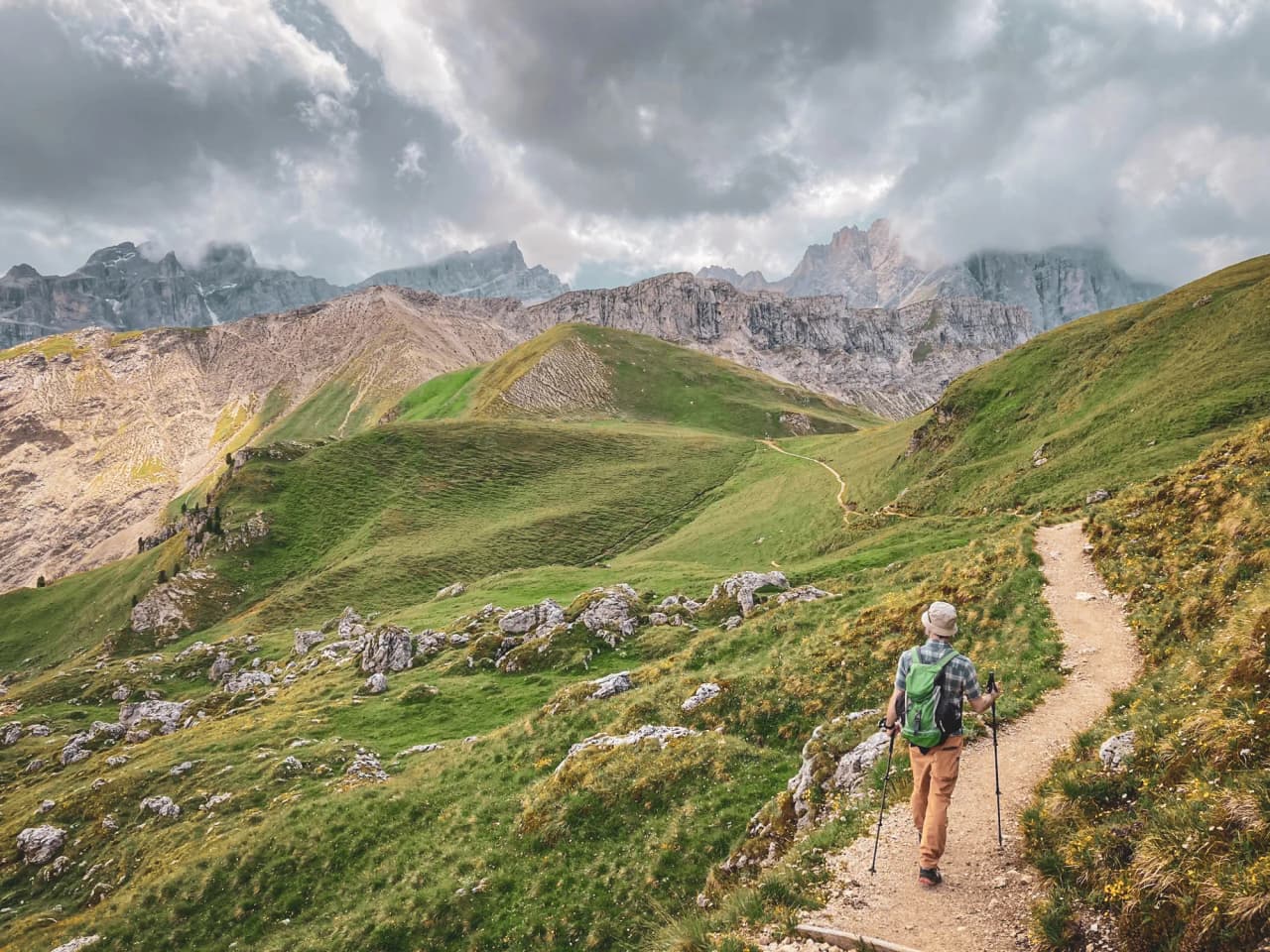 A solitary hiker on a green trail in the Dolomites, surrounded by majestic peaks.