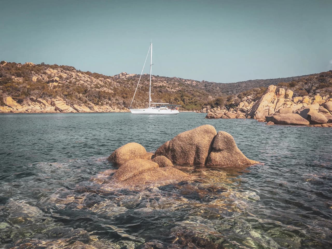 Bateau à voile bordant des criques rocheuses paisibles de la Corse du Sud, eaux cristallines.