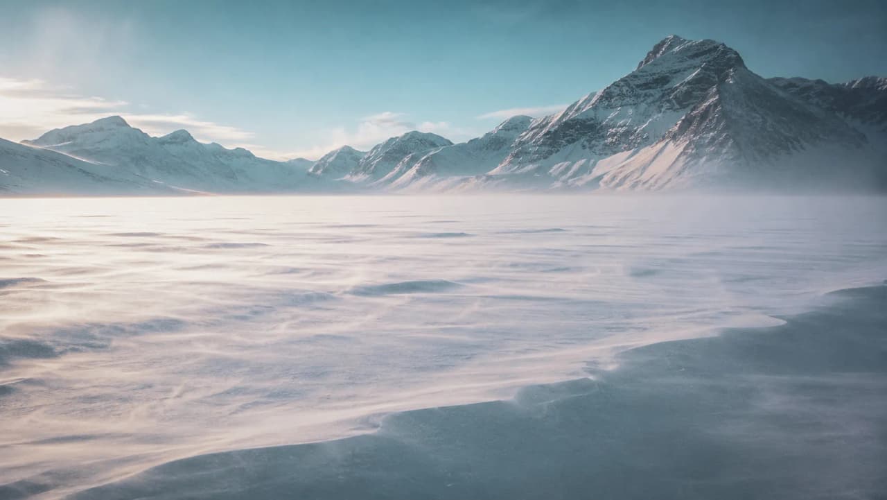 Een vredig arctisch landschap, besneeuwde bergen en een bevroren vlakte onder een helderblauwe hemel.