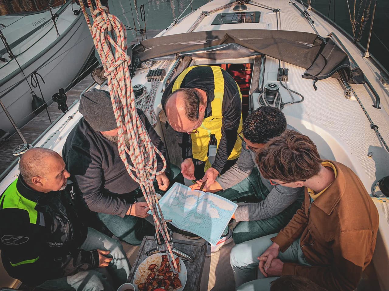 Een groep leerlingen op een zeilboot bestudeert zeekaarten om rond Zeeland te zeilen.