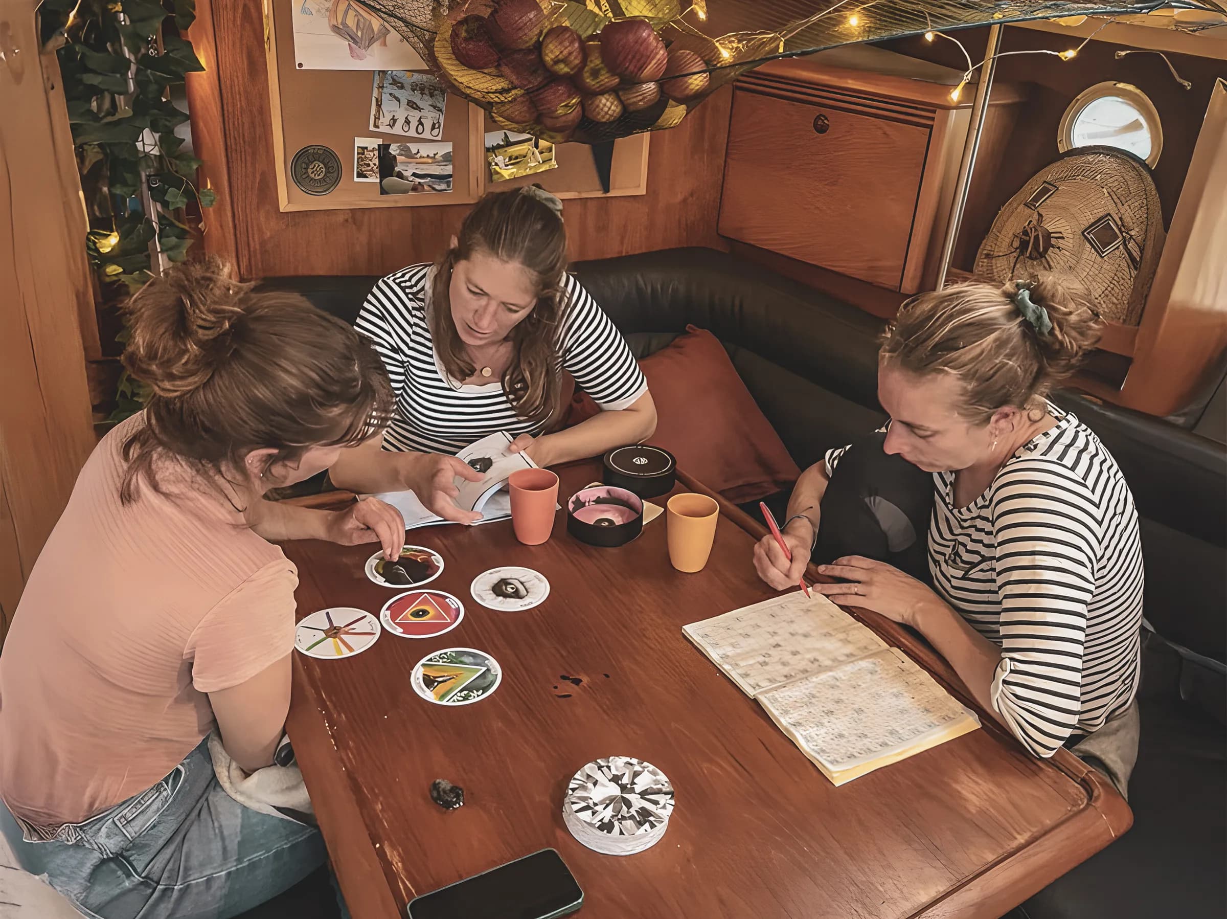 Trois femmes explorent la nature dans un bateau, entourées de cartes et de souvenirs marins.