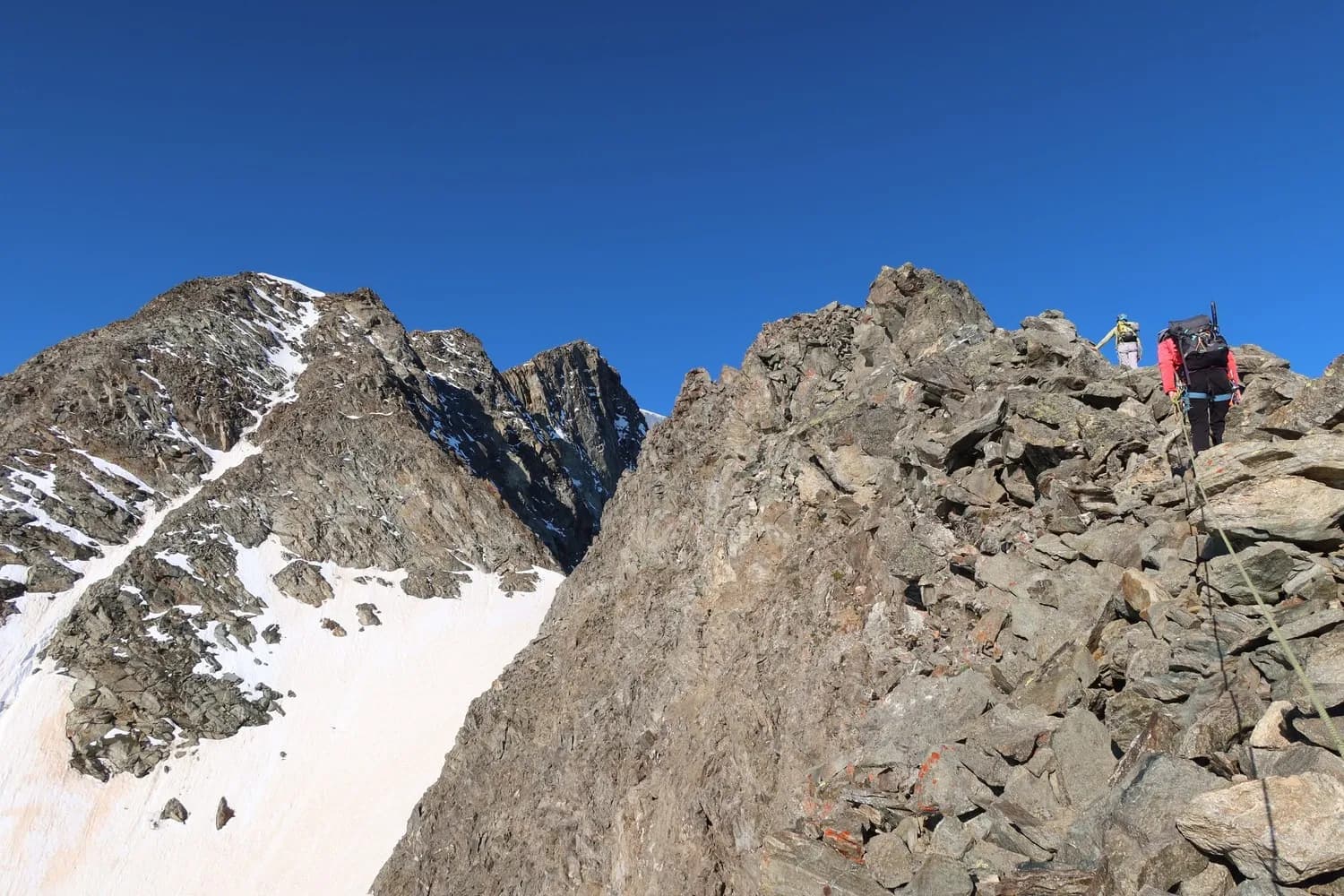 A group of hikers climbing a rocky ridge facing Mont Blanc under a brilliant sky.