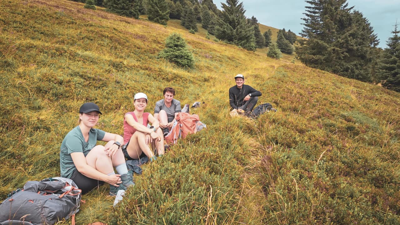 Quatre randonneurs se reposent sur une prairie verdoyante, entourés de forêts des Vosges.