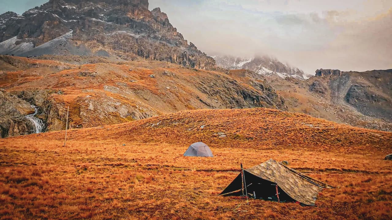 Un paysage de montagne à l'automne avec des tentes sous un ciel nuageux, invitant à l'aventure.