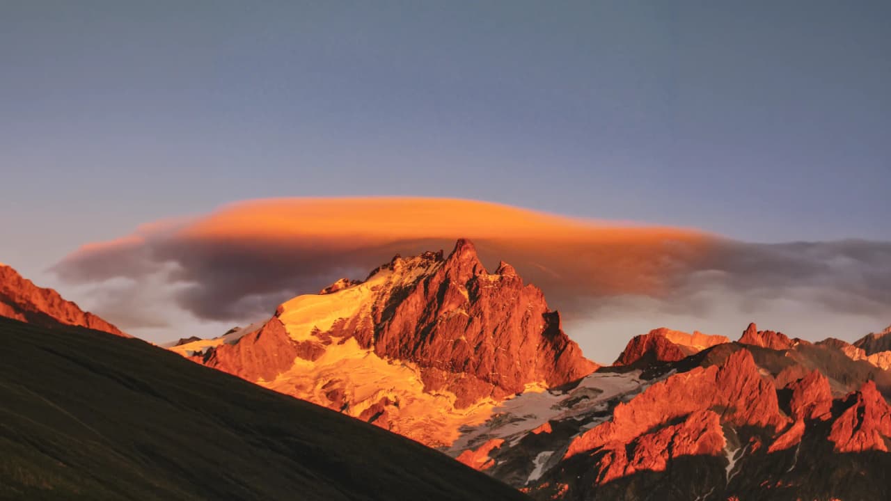 Montagnes majestueuses illuminées par le coucher de soleil, nuages flottants au-dessus des sommets.