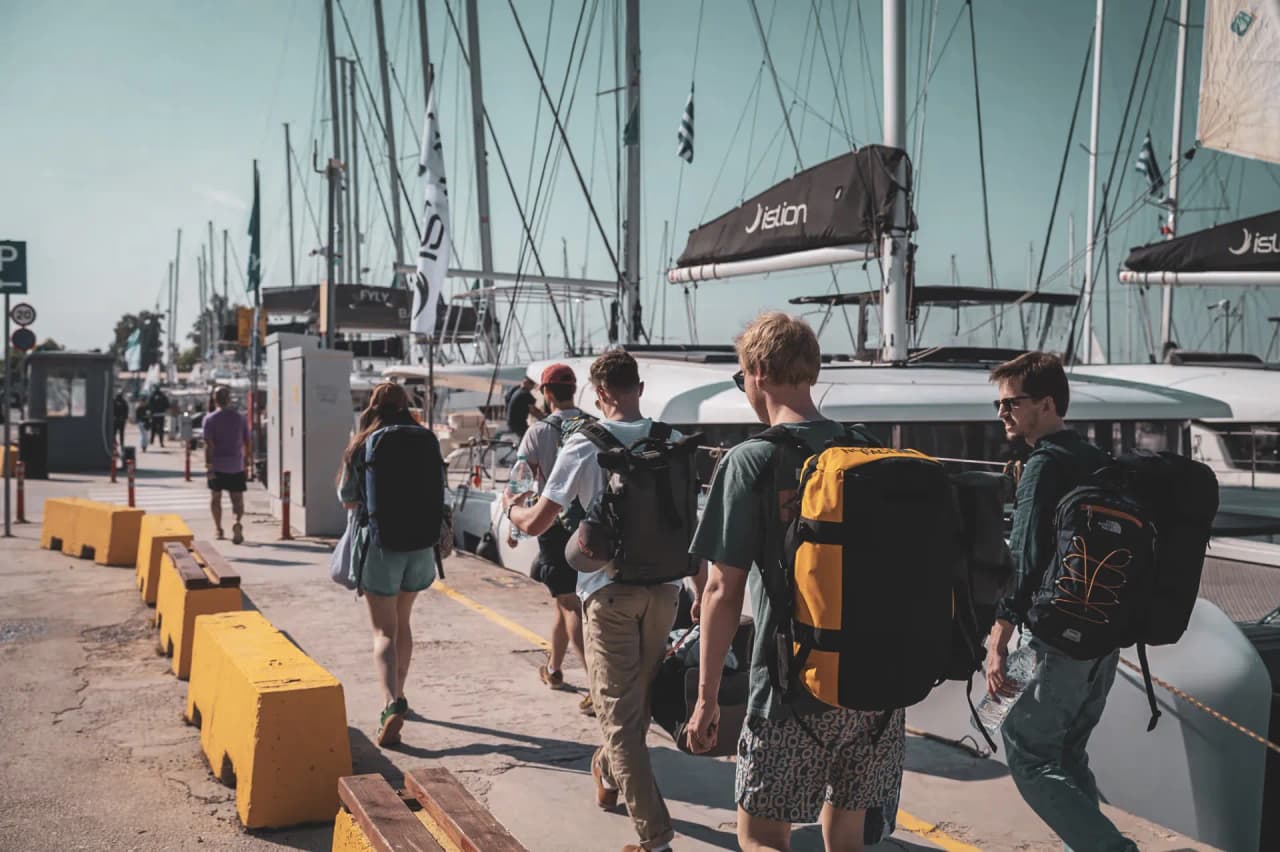 Un groupe de voyageurs se dirige vers des voiliers au port, prêt pour une aventure en mer.