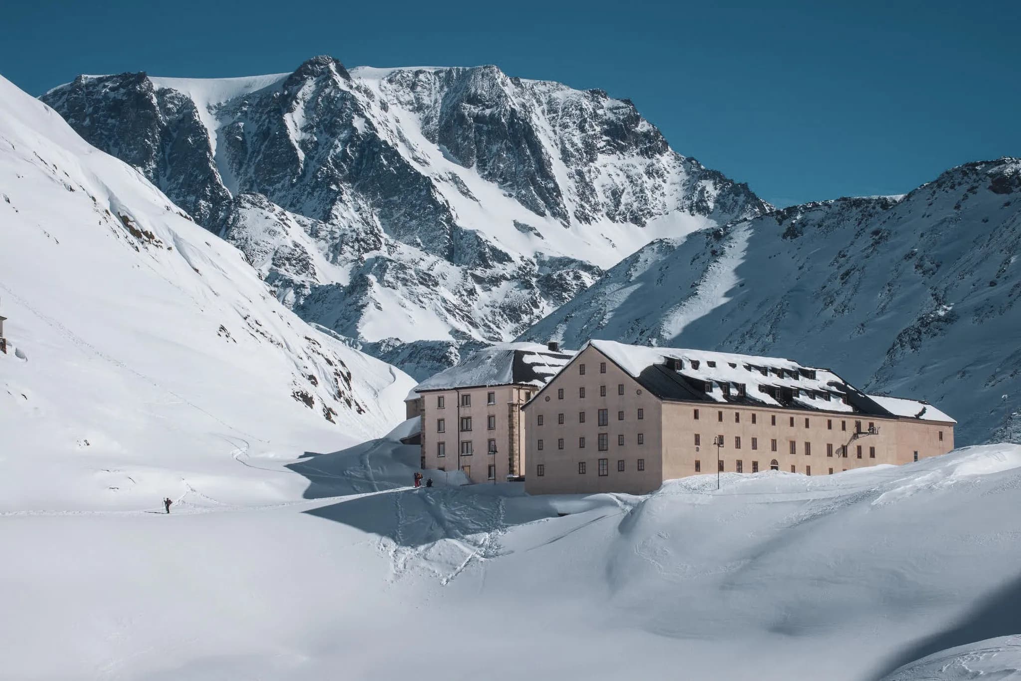 Mountain hut on the Great St Bernard Pass, surrounded by snow and majestic peaks.