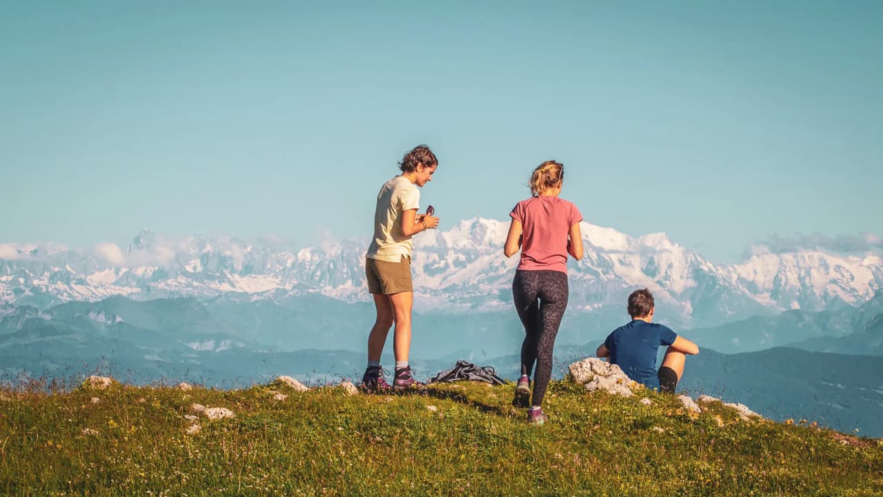 A group of hikers admiring the snow-capped Jura mountains under a sunny sky.