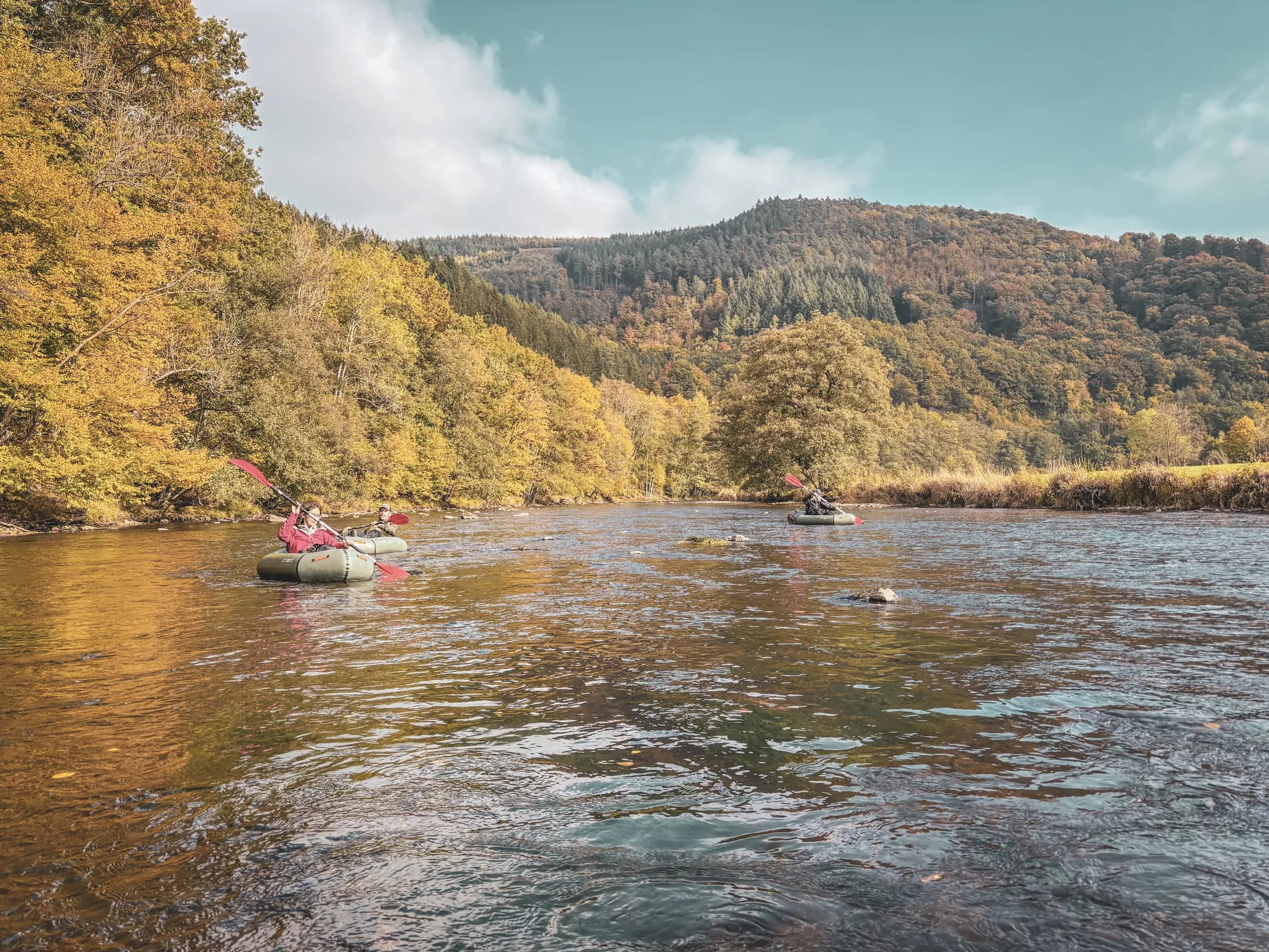 Adventurers in packraft sail peacefully down a river, surrounded by golden autumn forests.
