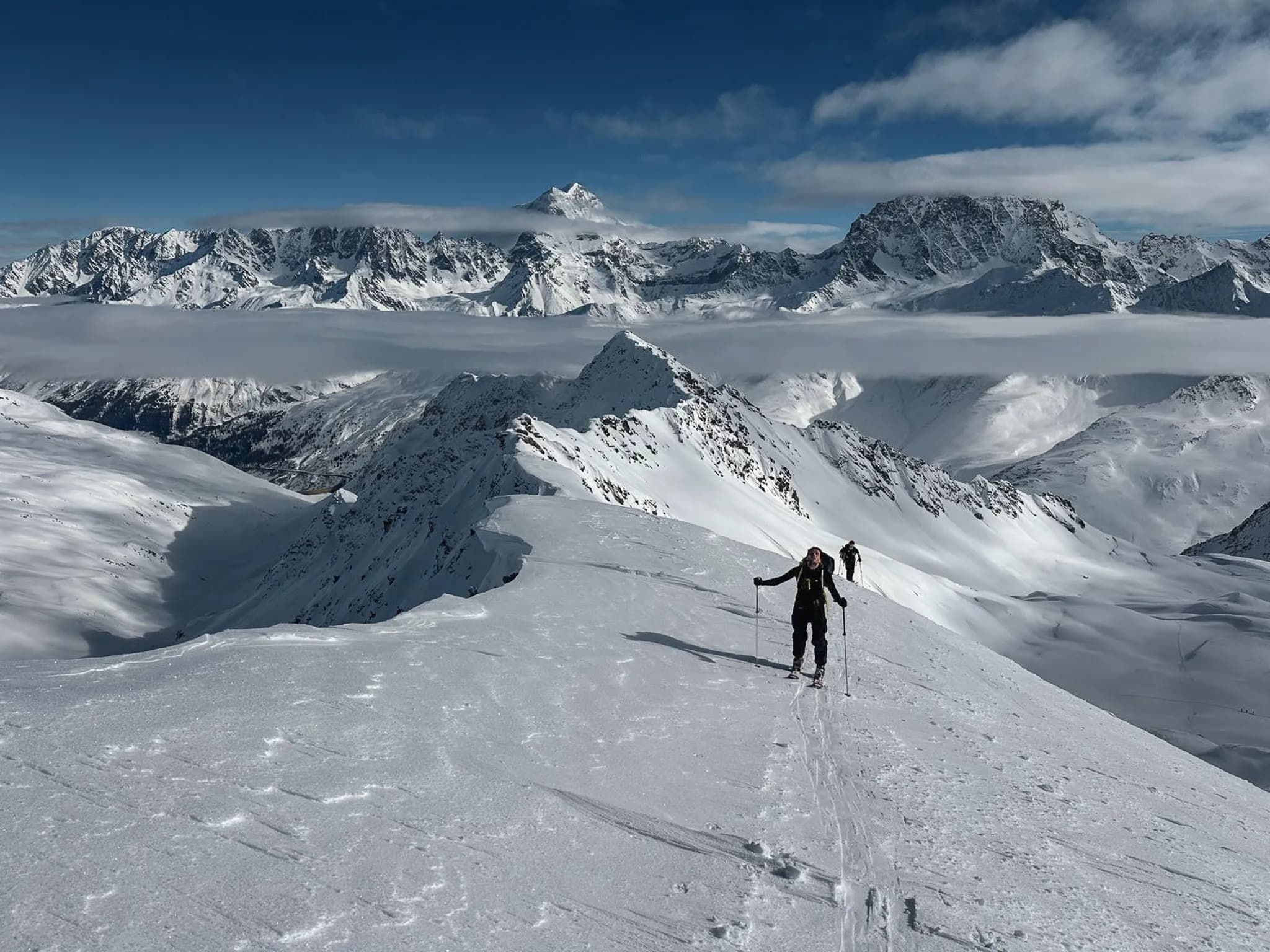 Ski touring on the Great St Bernard Pass, majestic Alpine scenery under a blue sky.