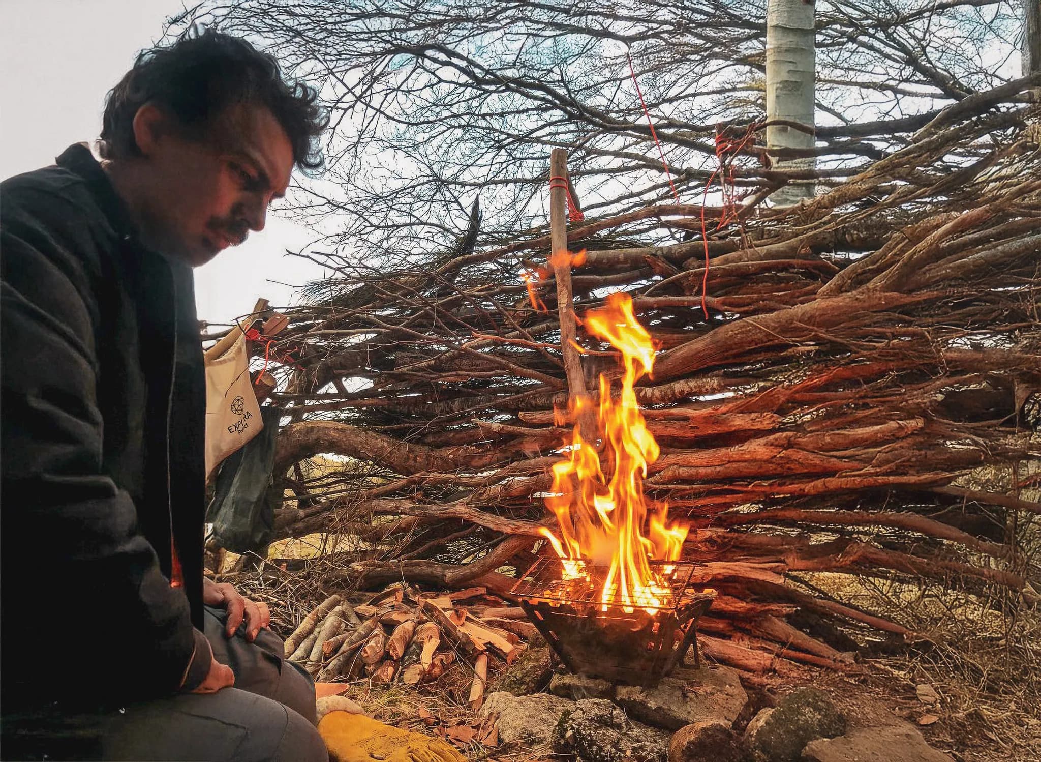 An attentive man in front of a campfire, a natural wooden shelter, a soothing atmosphere in the heart of nature.