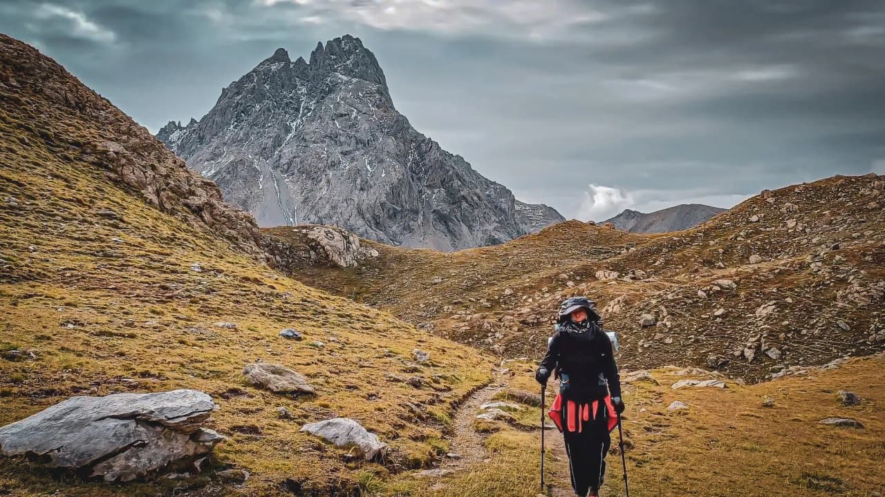 Randonneuse sur un sentier de montagne, avec des sommets majestueux en arrière-plan.