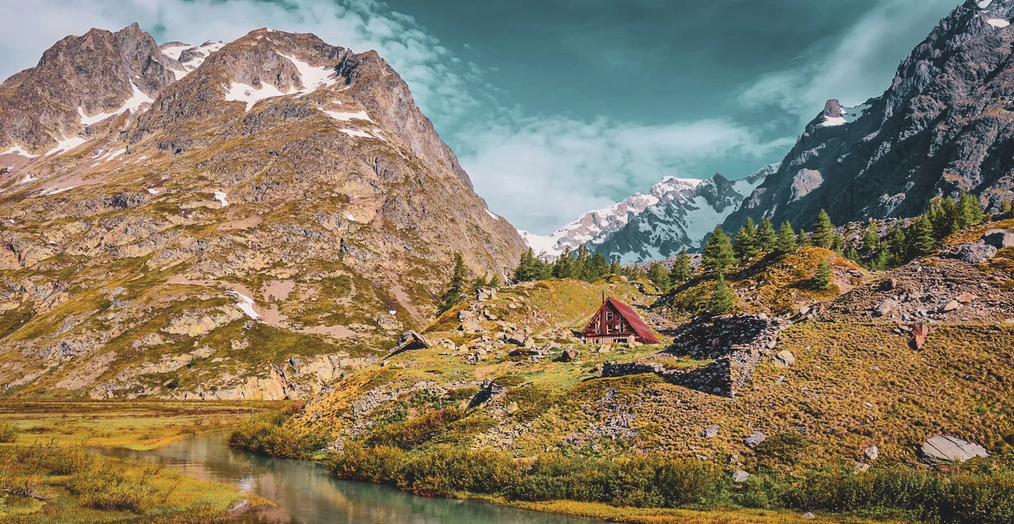 Un chalet en bois de style alpin se dresse sur une colline verdoyante, entouré de montagnes majestueuses, certaines recouvertes de neige. À proximité, une rivière sinueuse reflète le paysage environnant, tandis