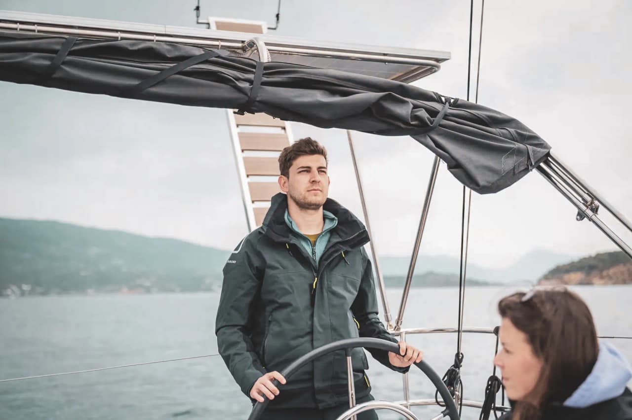 Un marin au volant d'un voilier, naviguant entre les îles grecques sous un ciel nuageux.