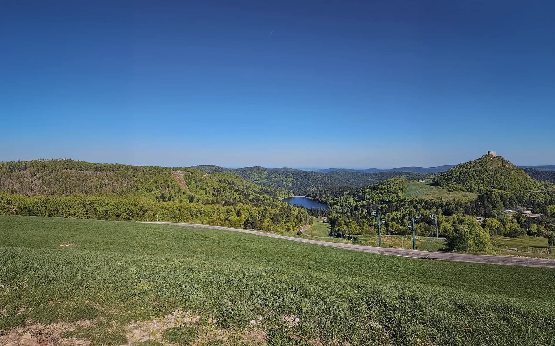 Panorama des Vosges avec lacs scintillants, forêts verdoyantes et ciel bleu éclatant.