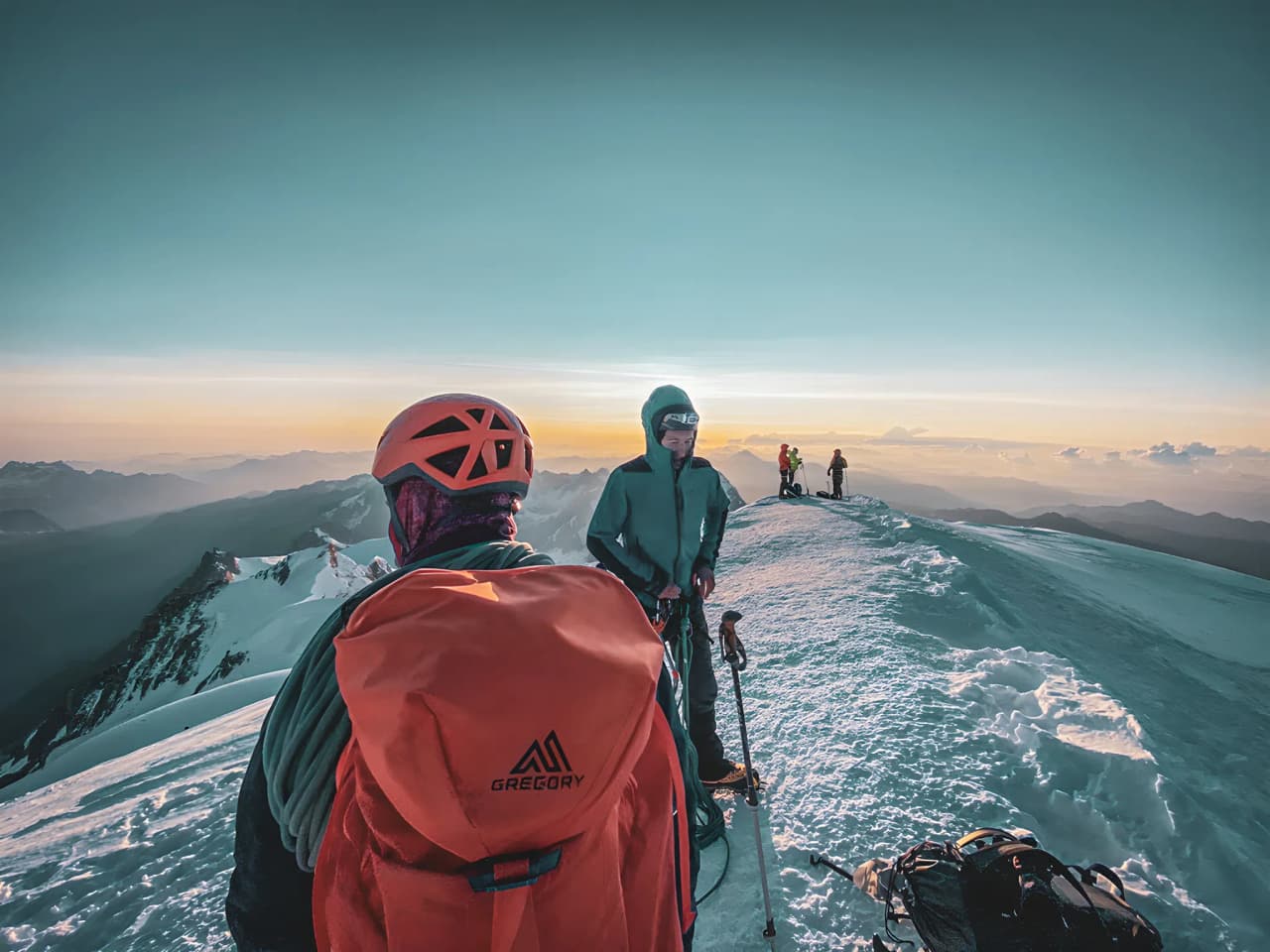 A group of climbers at the summit of Mont Blanc, under a magical orange sky at sunset.