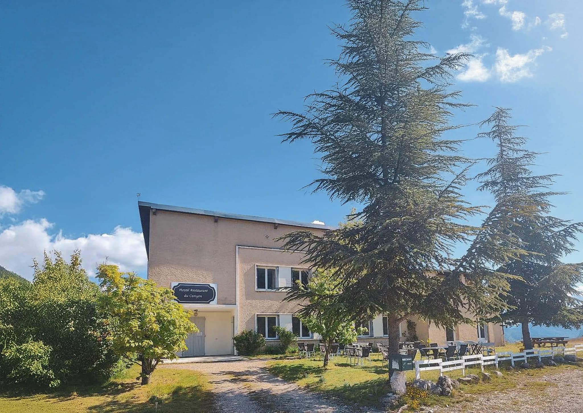A charming restaurant in the mountains, surrounded by greenery and under a brilliant blue sky.