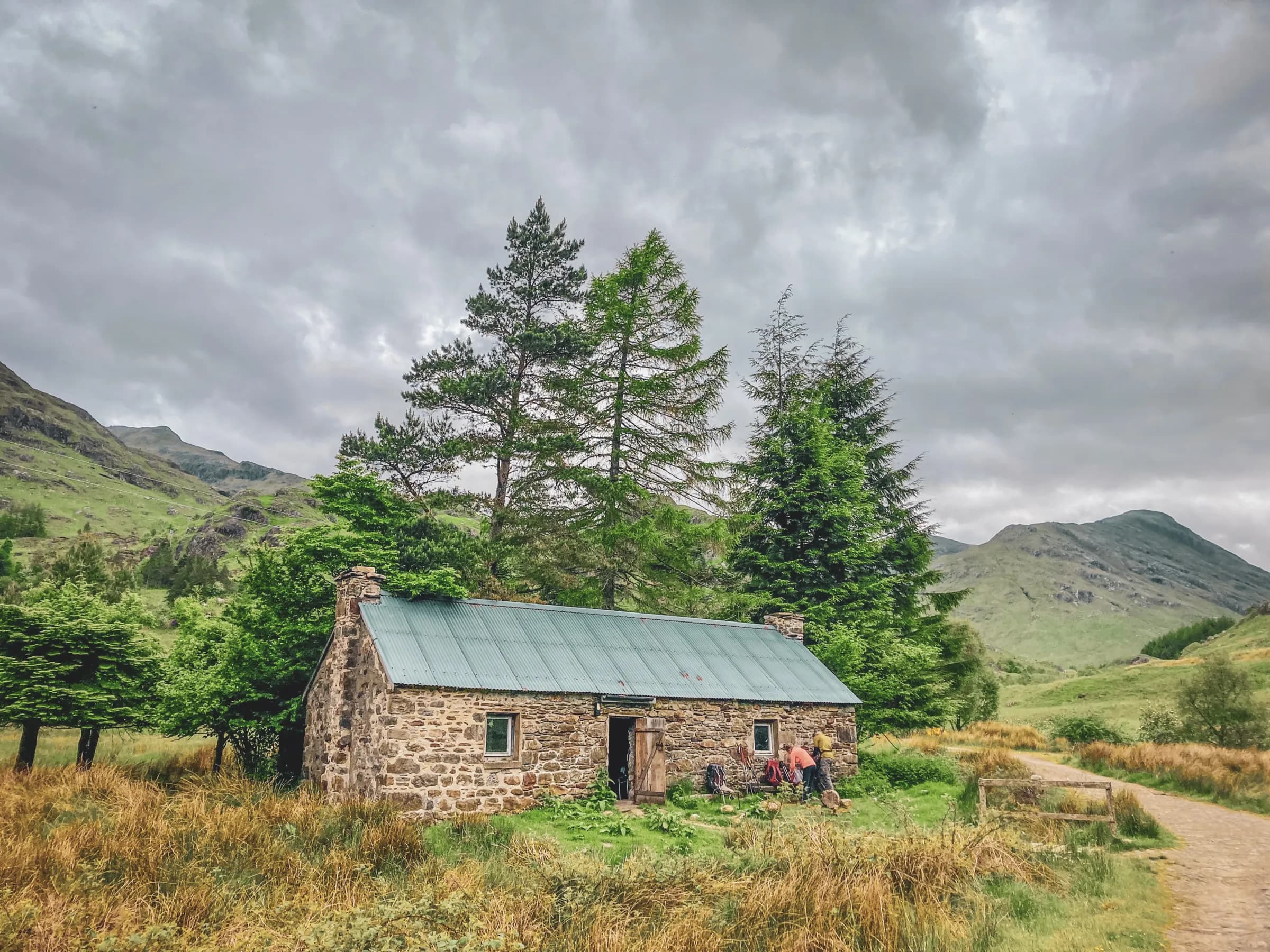 A stone cottage in the middle of the Scottish Highlands, surrounded by greenery and majestic mountains.