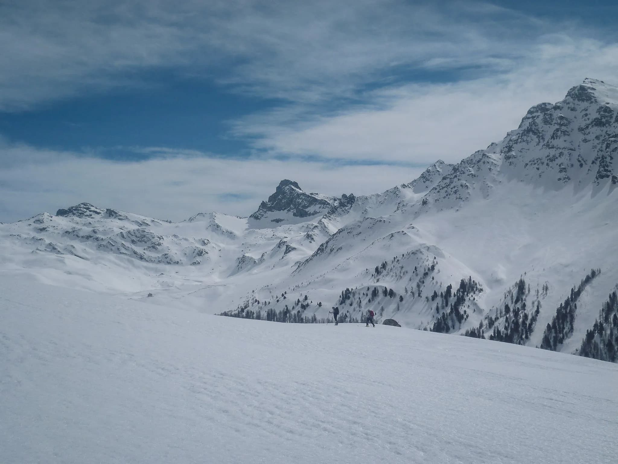 Snow-covered mountain landscape with skiers on a vast expanse of snow under a sunny sky.