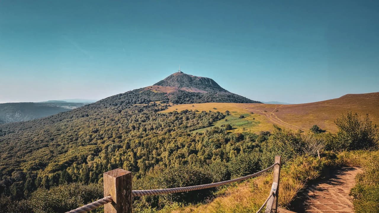 Panoramic view of Puy de Dôme, an iconic volcano surrounded by greenery and blue skies.