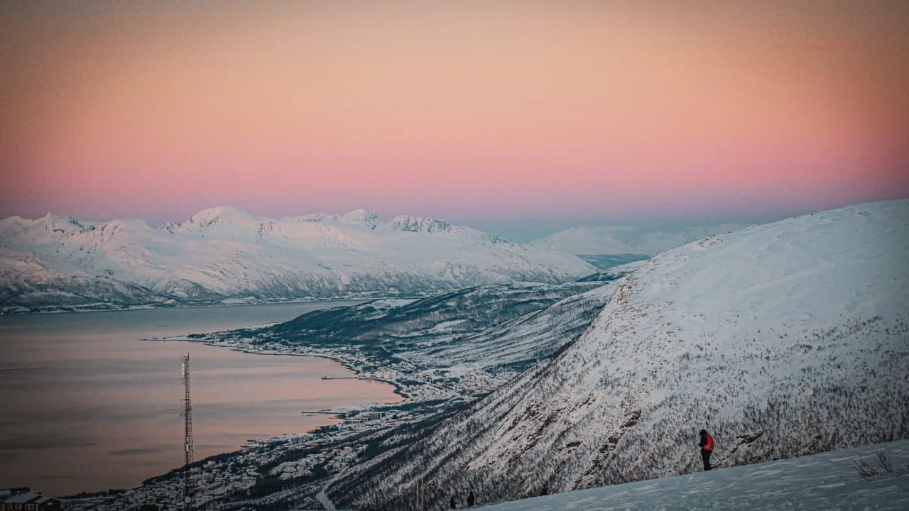 An enchanting panorama of the Tromsø fjords, beneath a pastel-coloured sky and a snow-covered landscape.
