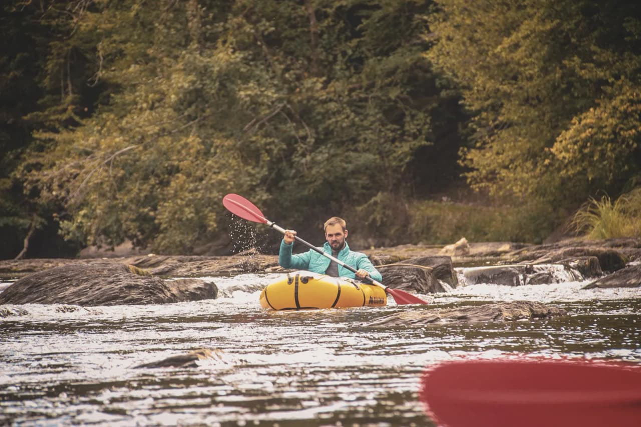 Een man peddelt in een rustige rivier, omgeven door wilde natuur in de Ardennen.