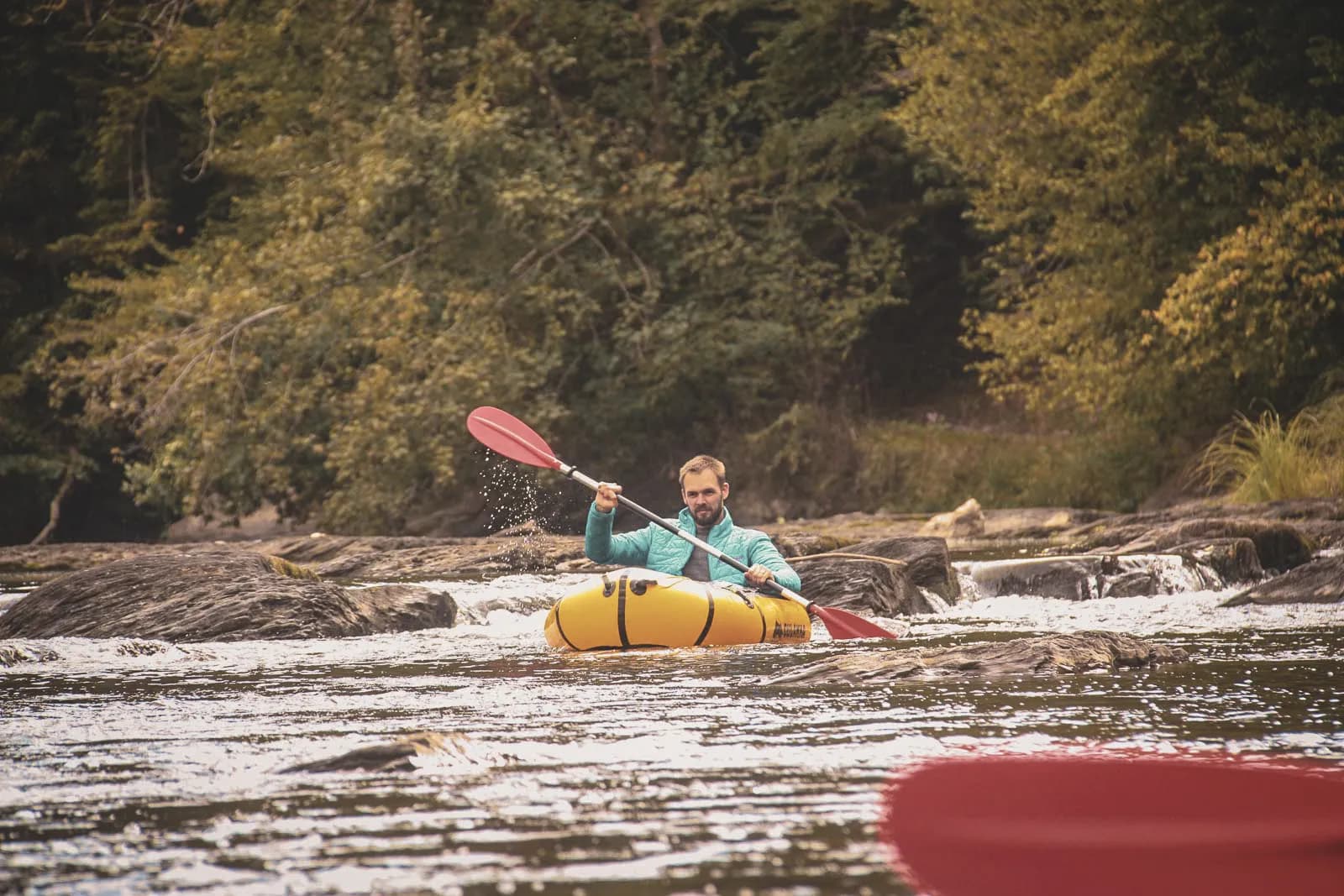 Een man peddelt in een rustige rivier, omgeven door wilde natuur in de Ardennen.