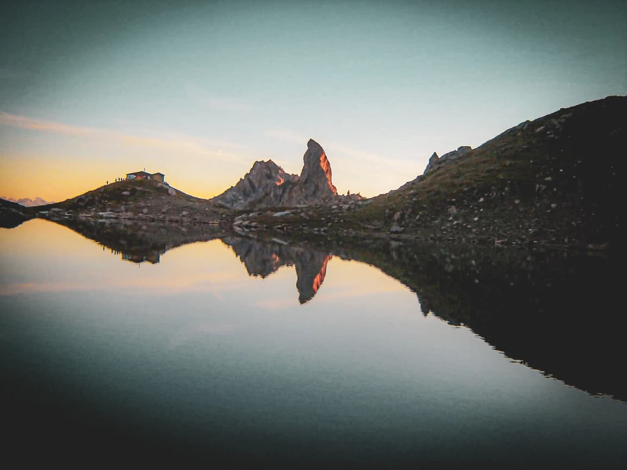 Lac paisible au coucher de soleil, montagne majestueuse, refuge pittoresque. Évasion alpine.