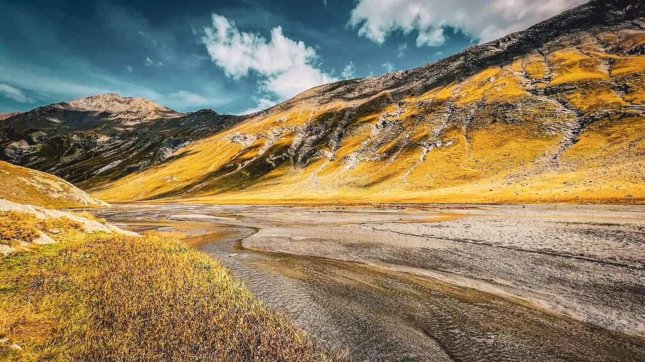Vaste paysage alpin avec des montagnes dorées sous un ciel bleu, invitant à l'aventure.