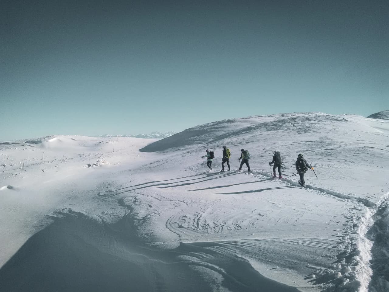 Groupe en raquettes avancent sur un vaste paysage enneigé du Jura suisse sous un ciel bleu.
