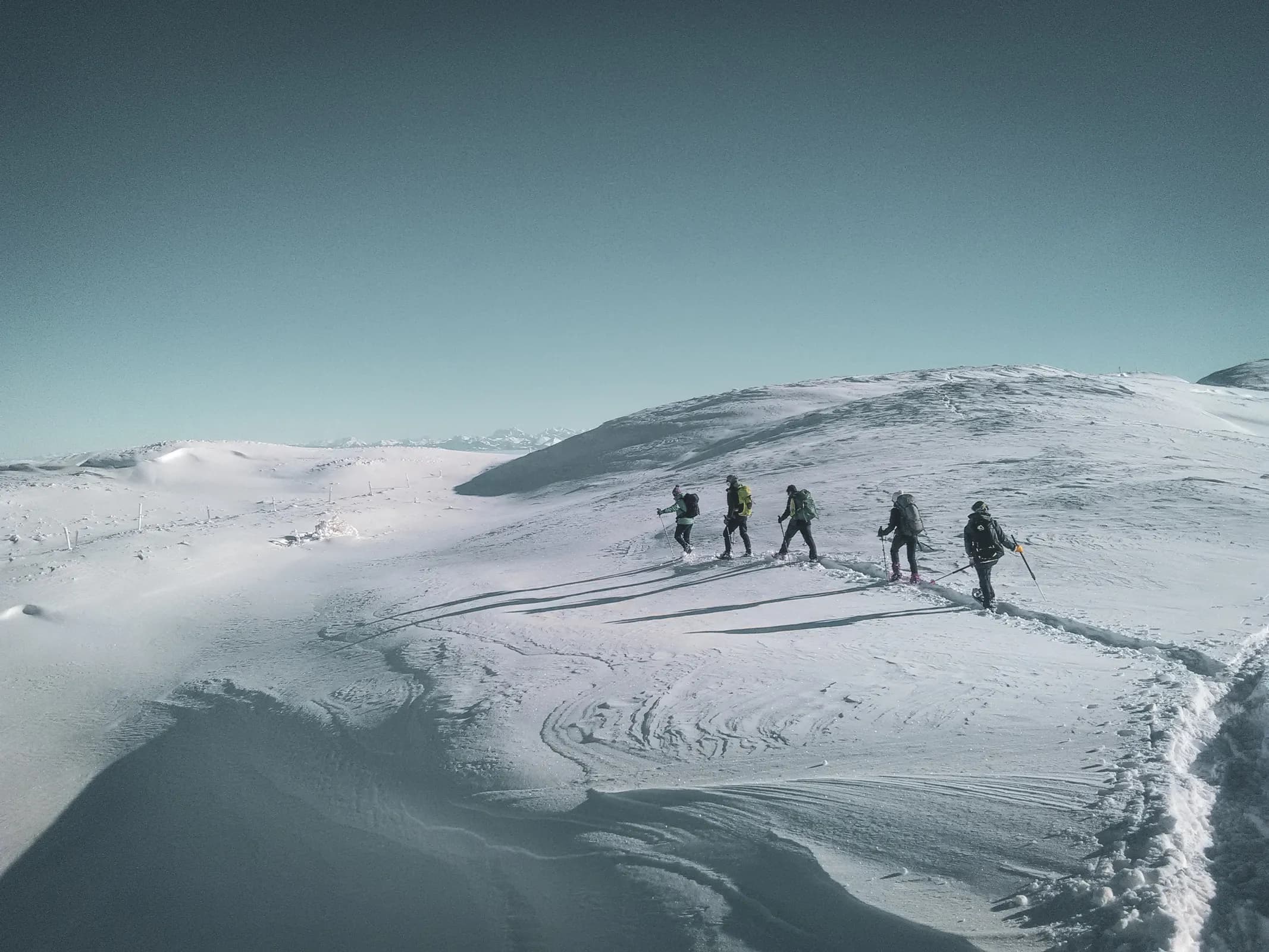Groupe en raquettes avancent sur un vaste paysage enneigé du Jura suisse sous un ciel bleu.
