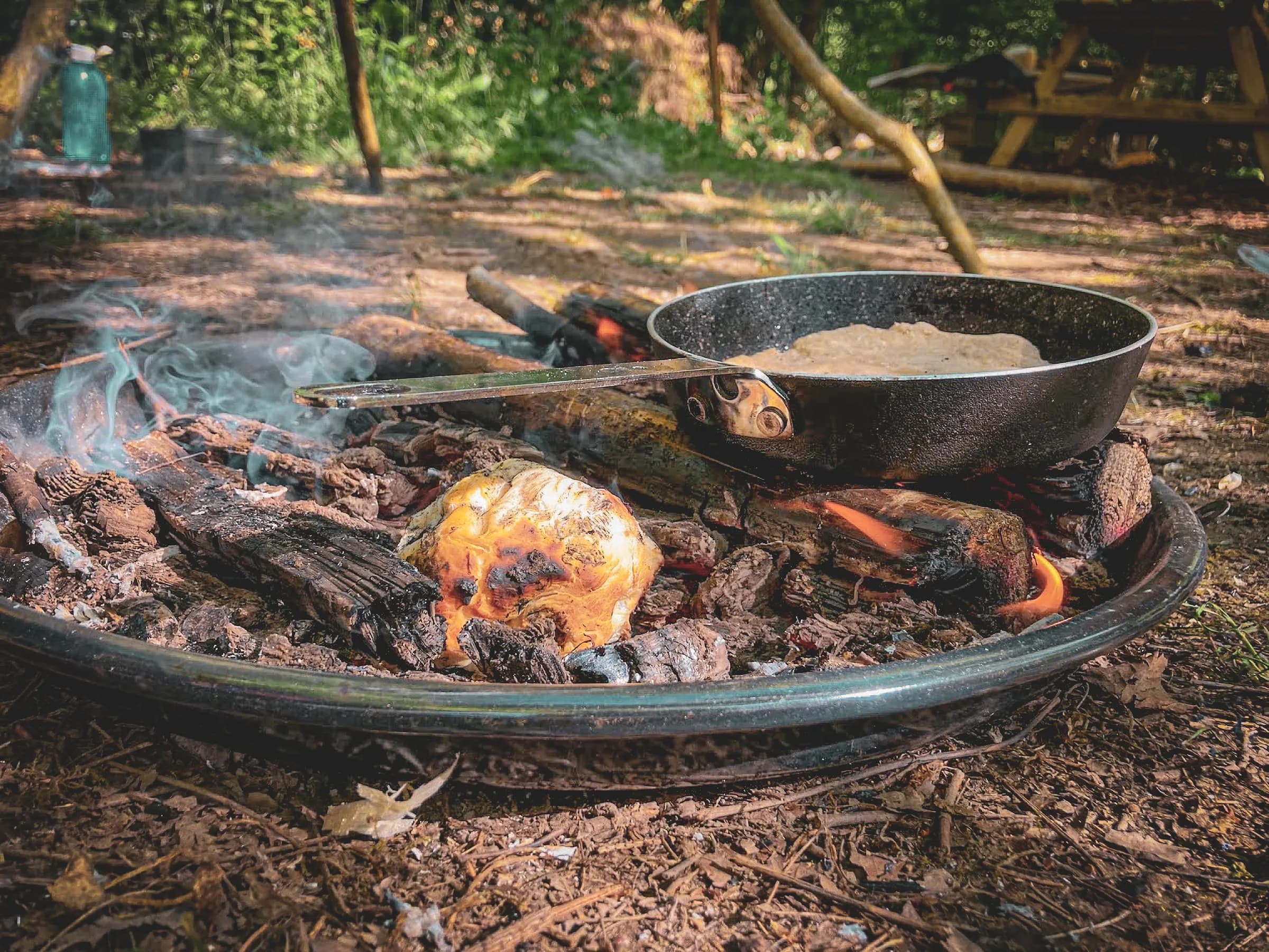 Een knapperend kampvuur met stukken hout en een koekenpan die staat te koken in the middle of nowhere.
