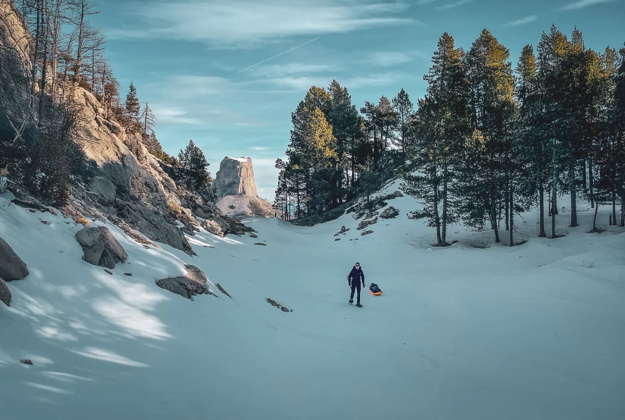Een avonturier op sneeuwschoenen doorkruist een besneeuwd landschap, omringd door majestueuze bergtoppen en bossen.