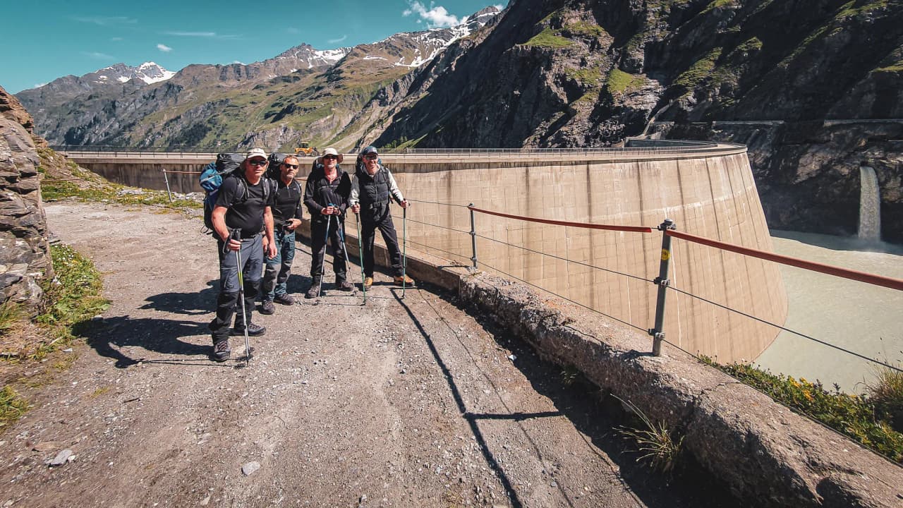 A group of hikers on the Haute Route, beside a glacial lake, with majestic mountains in the background.