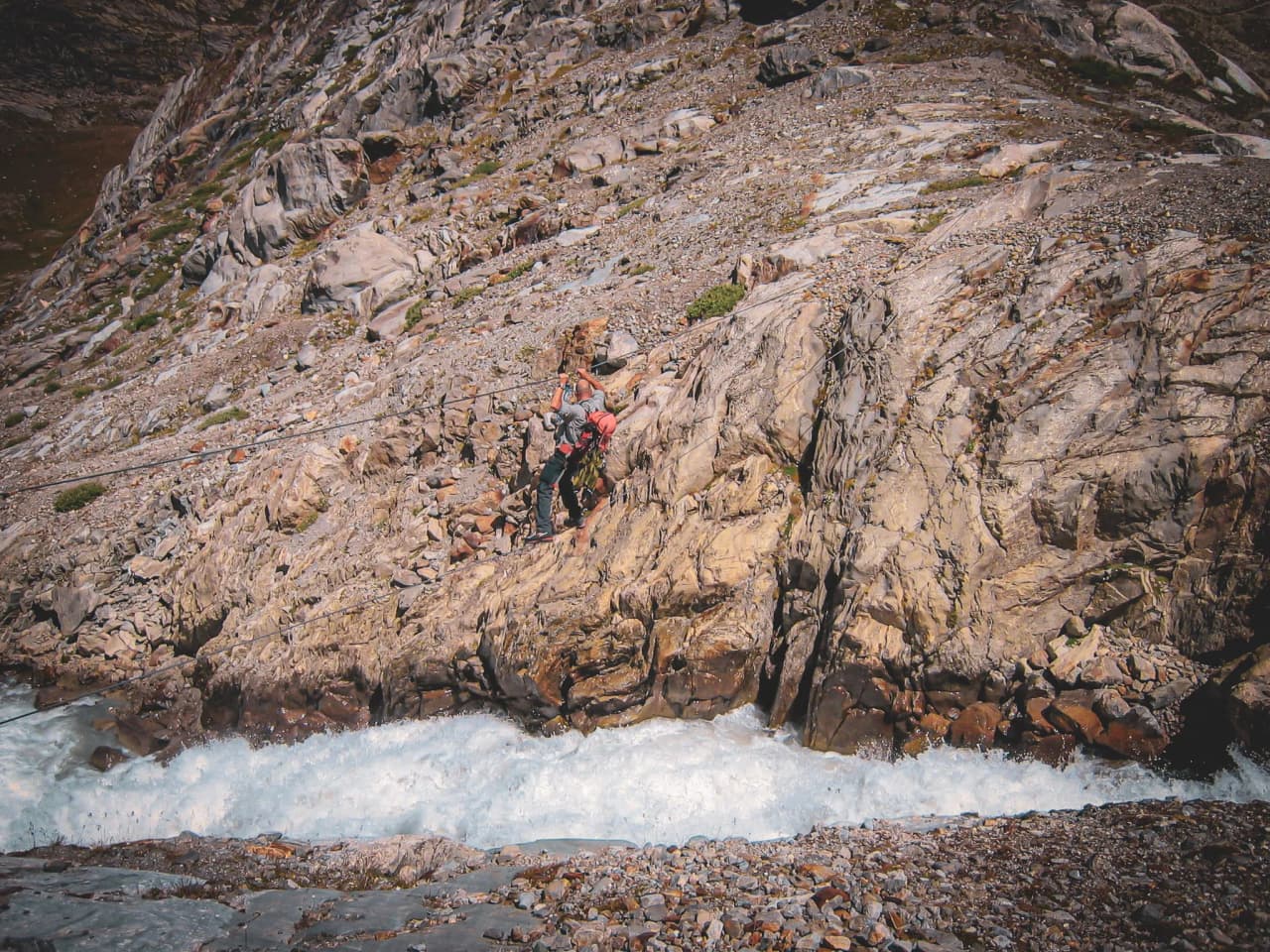 Grimpez sur des rochers escarpés au bord d'un glacier, avec une rivière tumultueuse en contrebas.