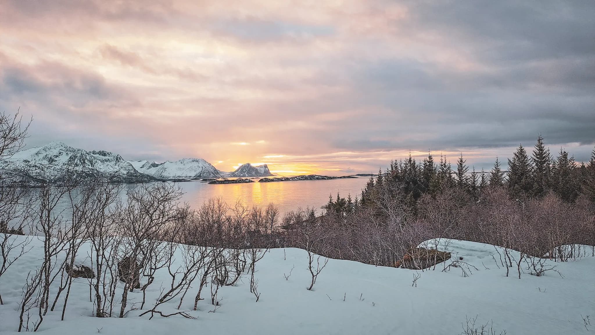 An enchanting panorama of snow-capped mountains and calm sea at sunset, on the island of Senja.