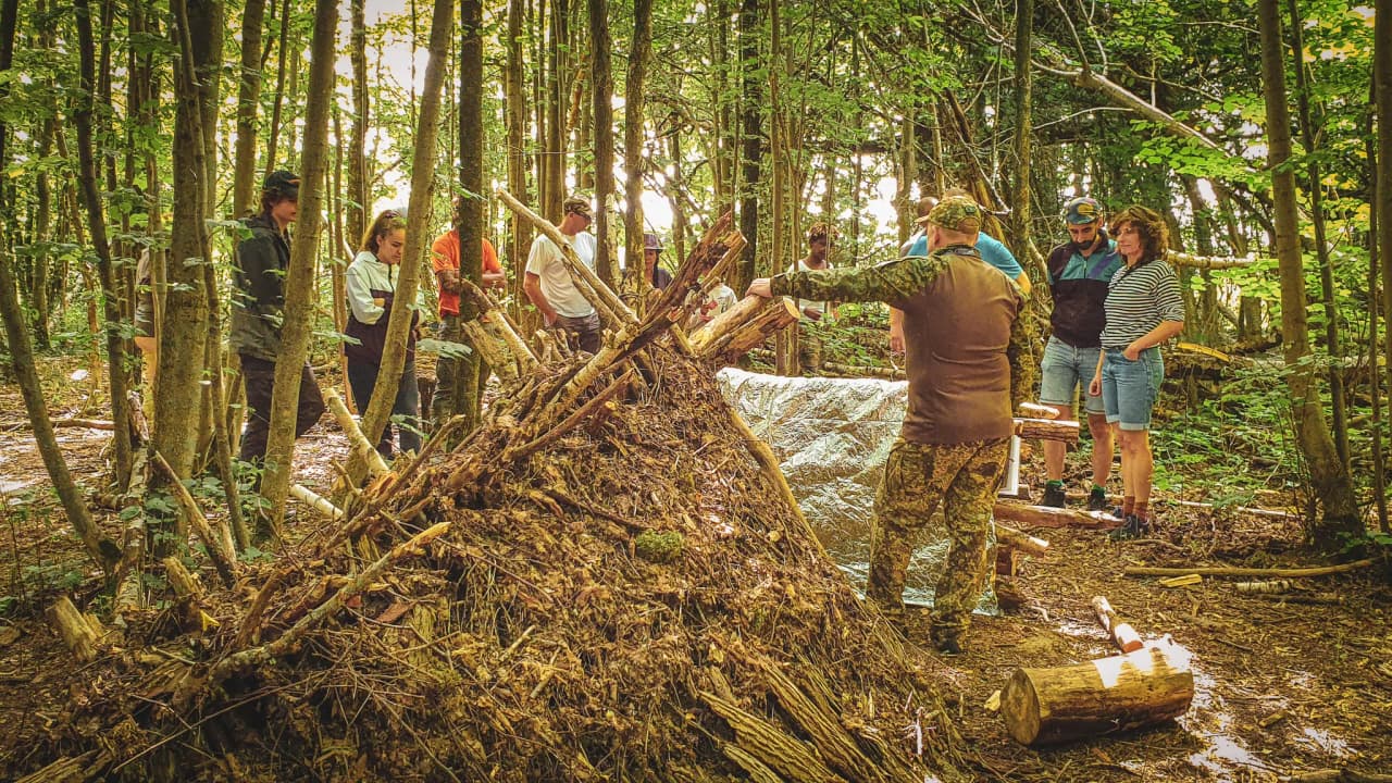 Groupe en pleine nature, apprenant à construire un abri en bois lors d'un stage de survie.