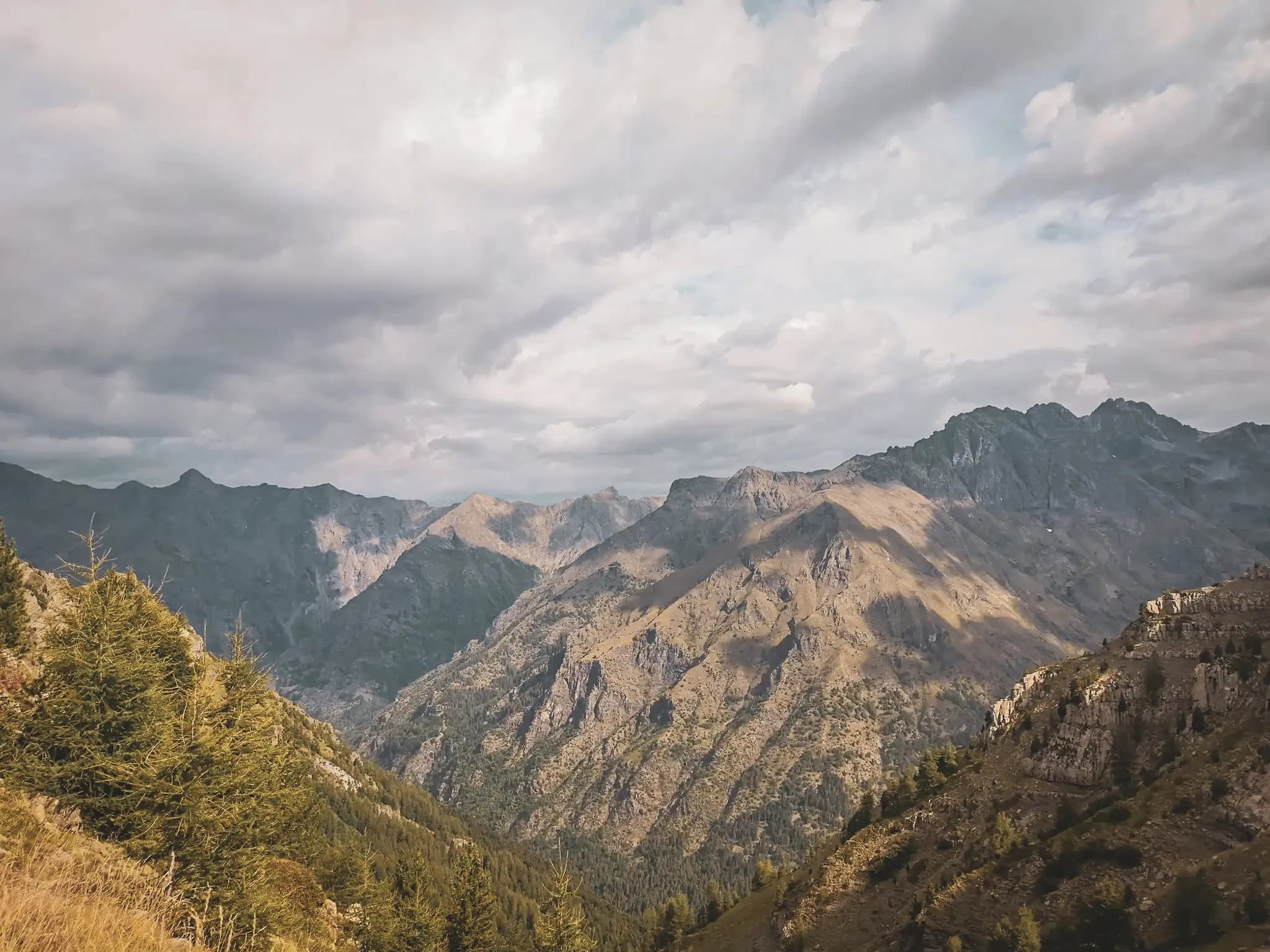 A majestic view of the Écrins mountains, combining greenery and cloudy skies, a call to adventure.