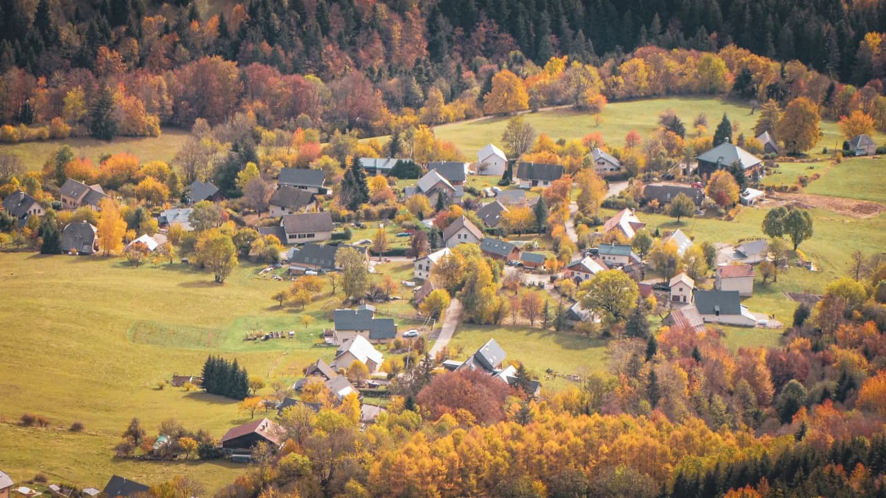 Un village paisible entouré d'arbres aux couleurs automnales, idéal pour une escapade en nature.