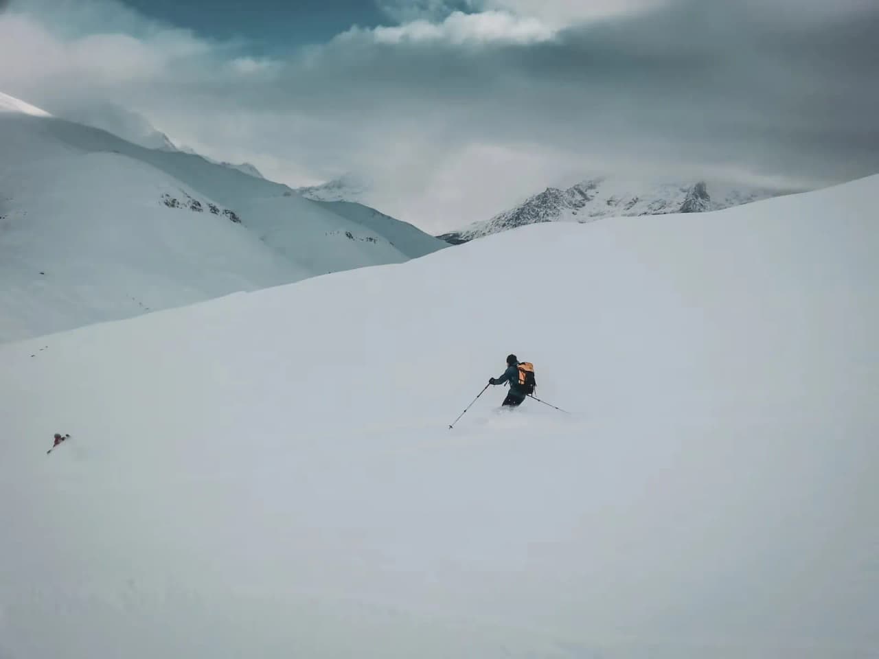 Skieur en pleine descente sur un vaste champ de neige, montagnes majestueuses en arrière-plan.