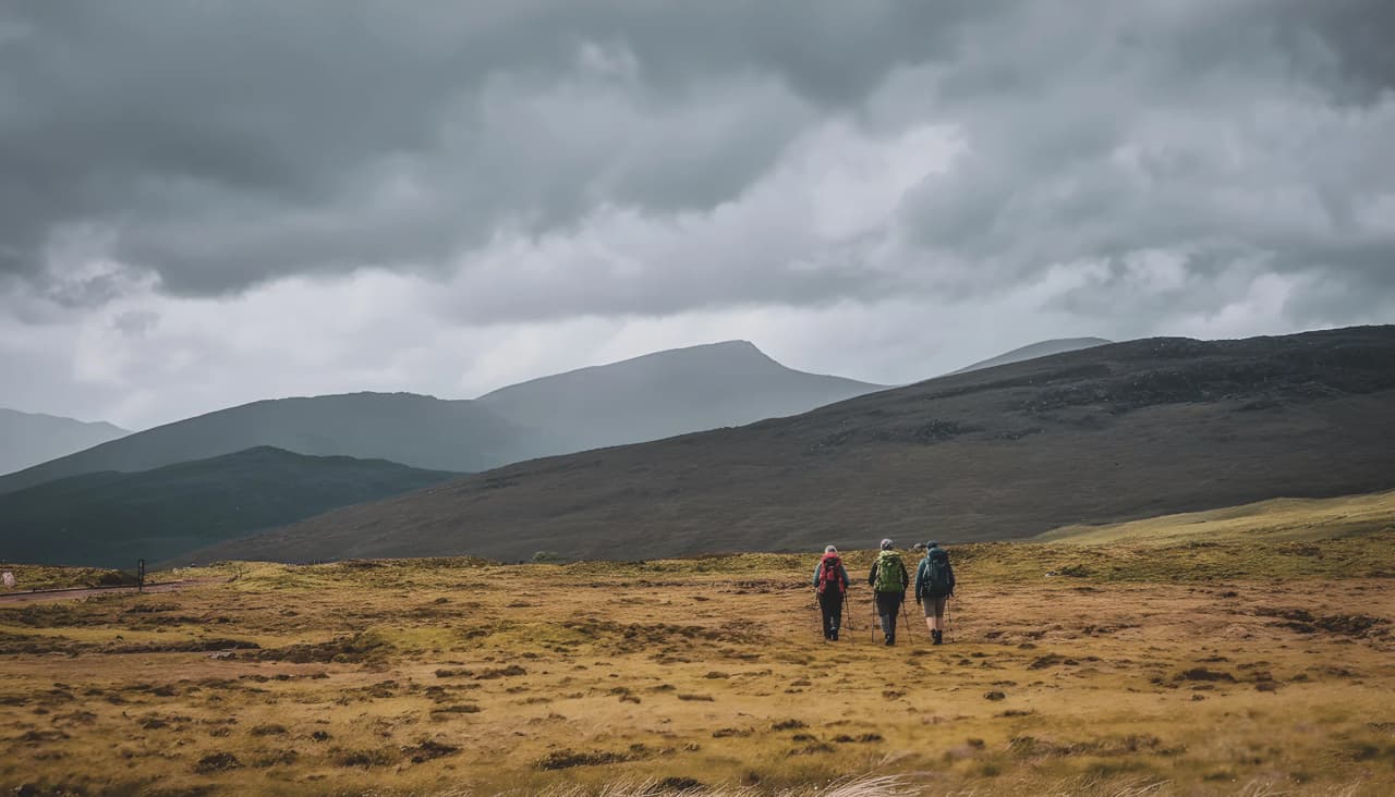 Three walkers make their way through the Scottish Highlands under dramatic skies.