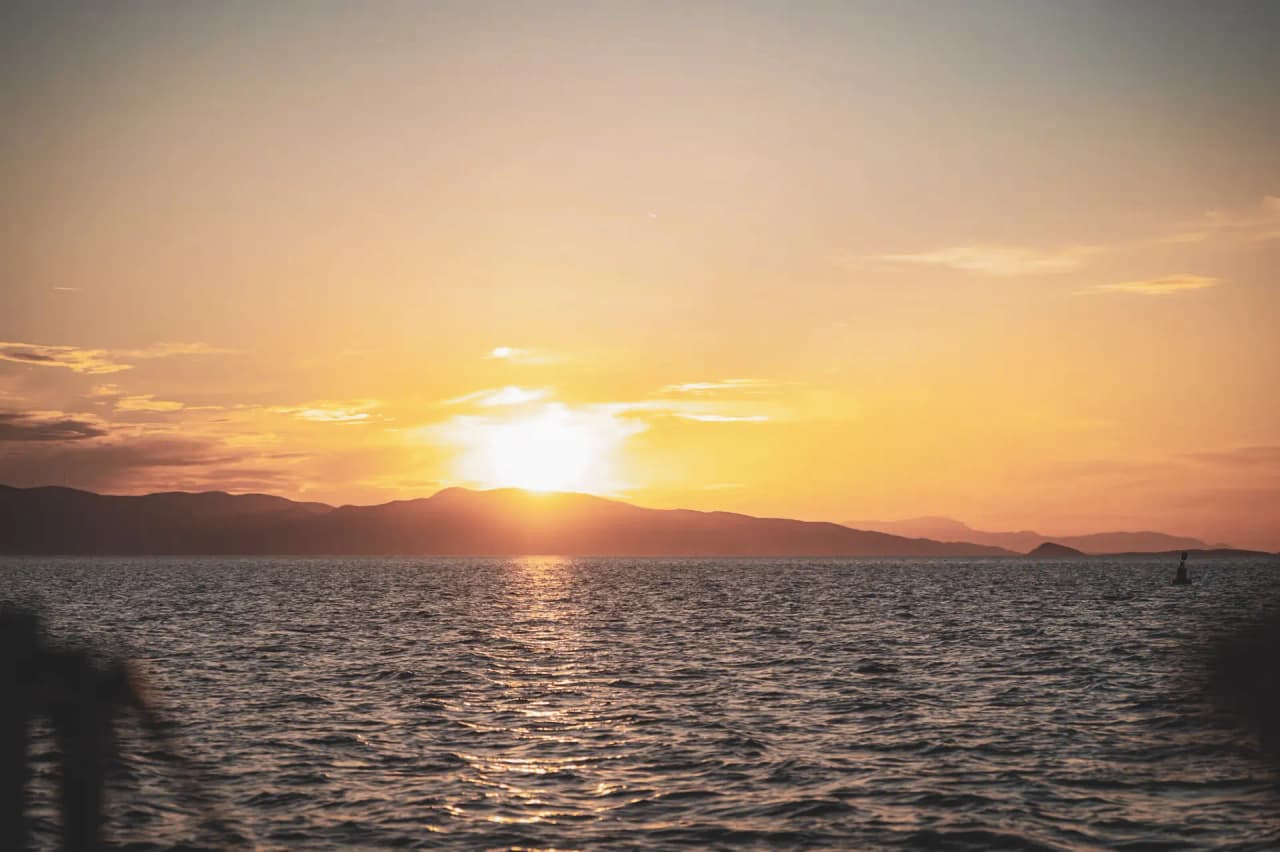 Coucher de soleil sur la mer, montagnes en arrière-plan, ambiance paisible de voyage méditerranéen.